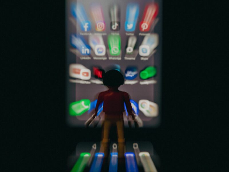 Photo of a plastic figurine in front of a smartphone displaying social media icons