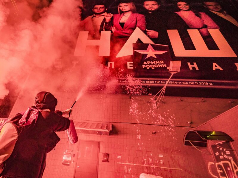 Photo of a protestor throwing red paint on the banner of the TV channel NASH to protest against Russian propoganda