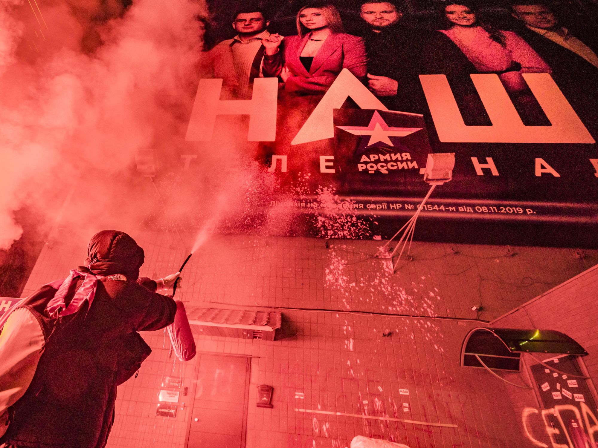 Photo of a protestor throwing red paint on the banner of the TV channel NASH to protest against Russian propoganda