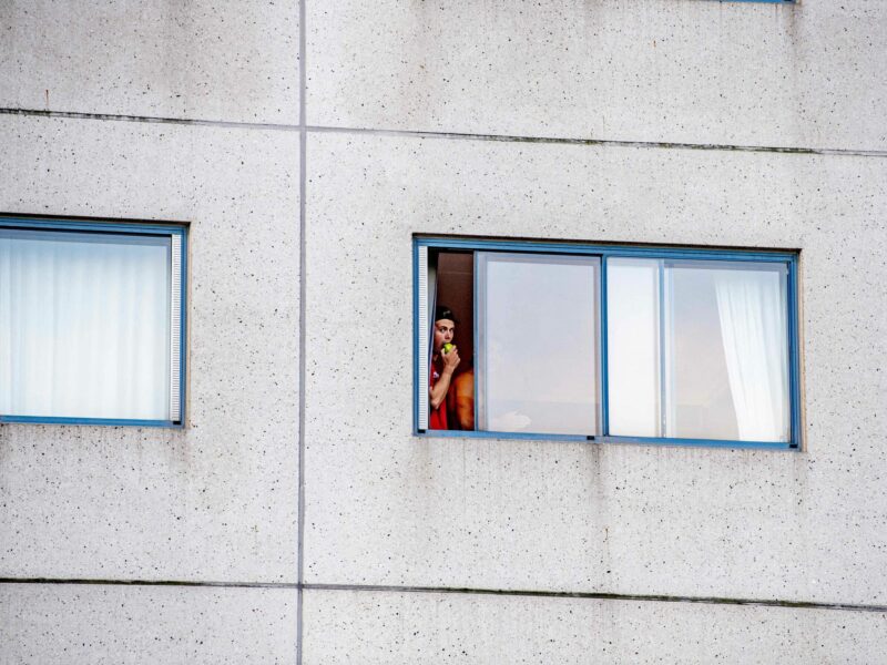 Photo of a quarantined traveler looking out the window of a hotel at Amsterdam's Schiphol airport