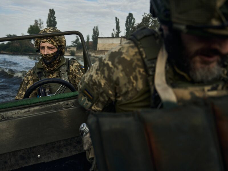 photo of a soldier driving a boat on a river
