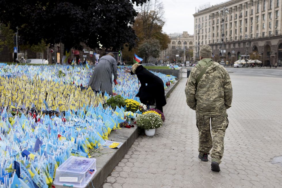 photo of a soldier walking past a memorial of small ukrainian flags