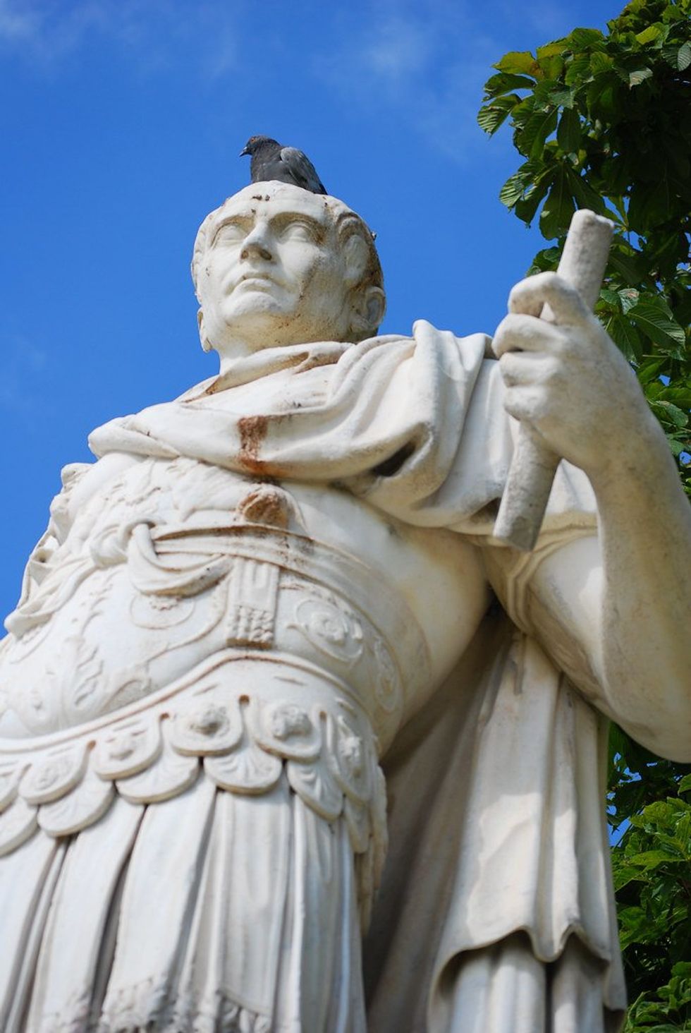Photo of a statue of Julius Caesar shot from below, with a pigeon on its head