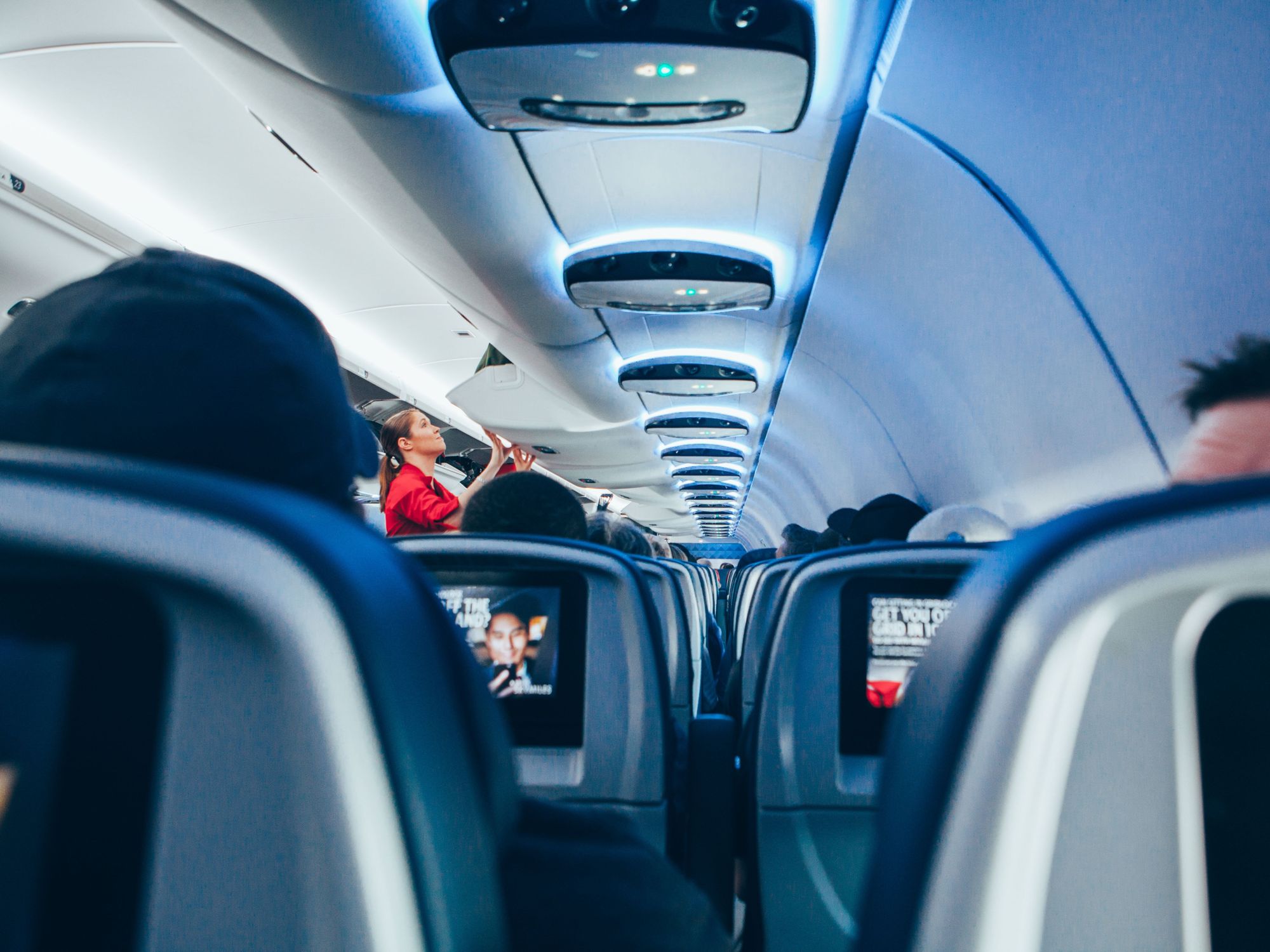 Photo of a stewardess loading up luggage in an overhead compartment of a plane