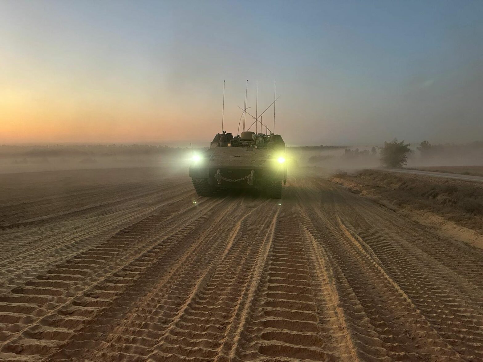 photo of a tank in the desert with its headlights on