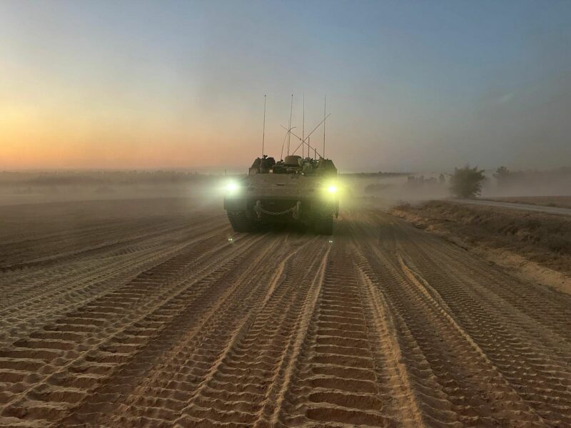 photo of a tank in the desert with its headlights on
