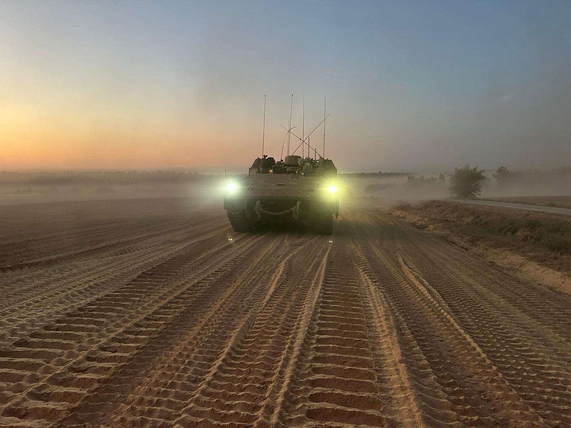 photo of a tank in the desert with its headlights on