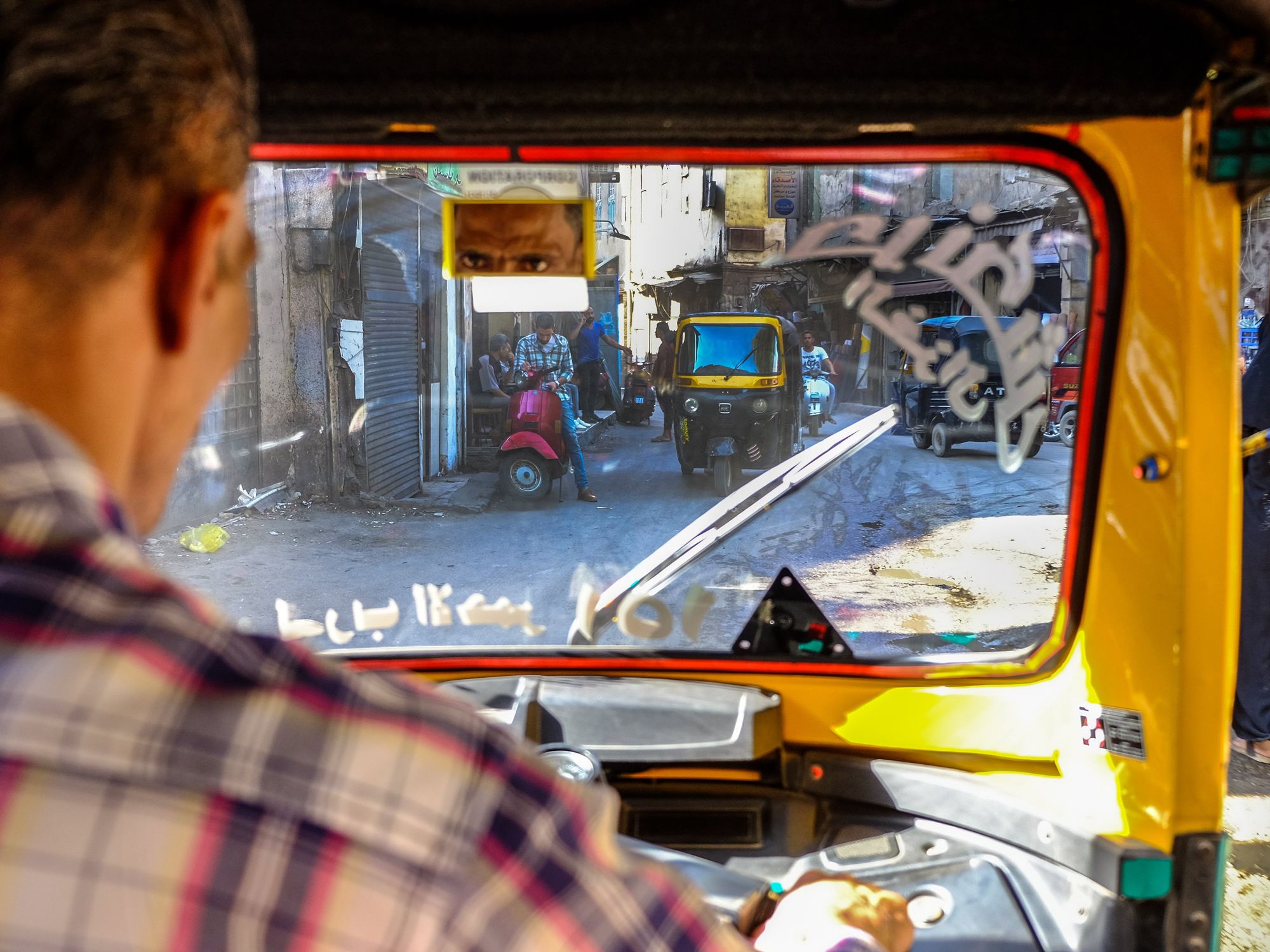 Photo of a tuk-tuk driver looks in his rearview mirror, in Cairo