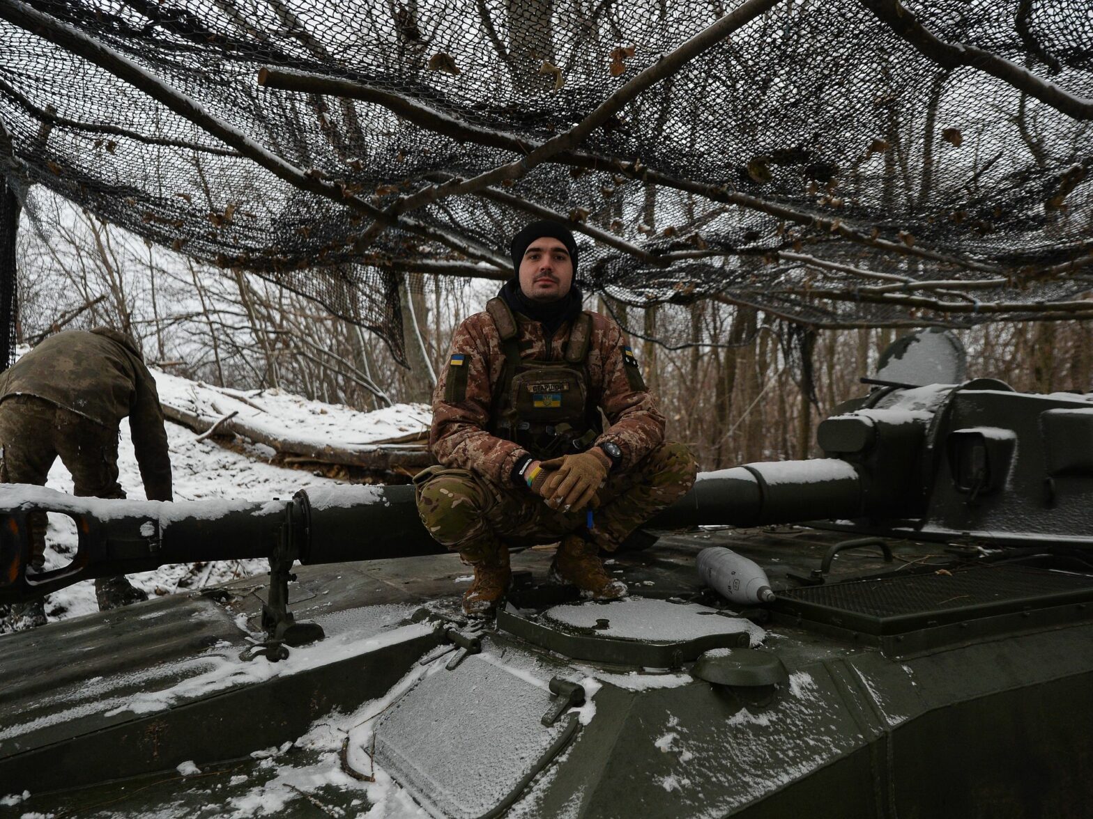 Photo of a Ukrainian soldier crouching on a tank near Kyiv in a snowy landscape