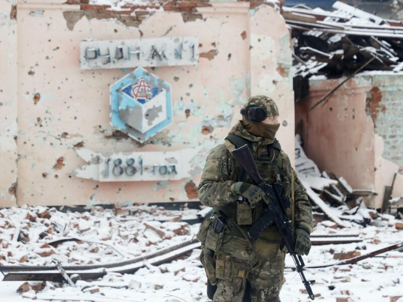 Photo of a Wagner Group fighter in front of a destroyed building in the snow