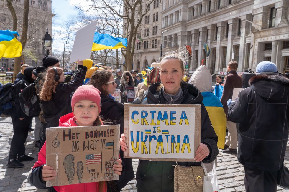 Photo of a woman and her daughter holding signs saying "NO WAR" and "CRIMEA IS UKRAINA"