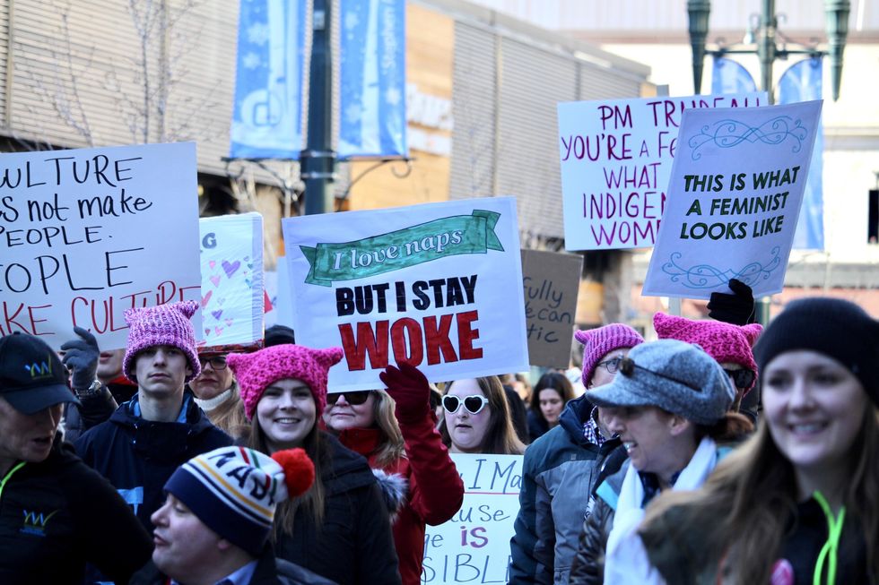 Photo of a woman carrying placard reading "i love naps but i stay woke" during a feminist march in Calgary, Canada