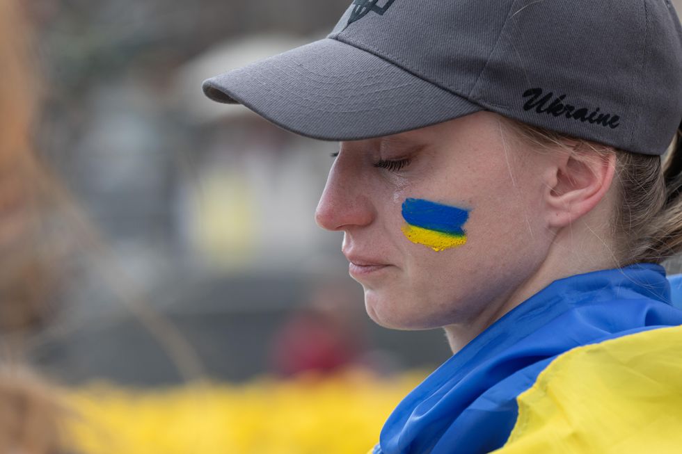 Photo of a woman crying, with a ukrainian flag painted on her left cheek, as she participates in a gathering on Kyiv's independence square