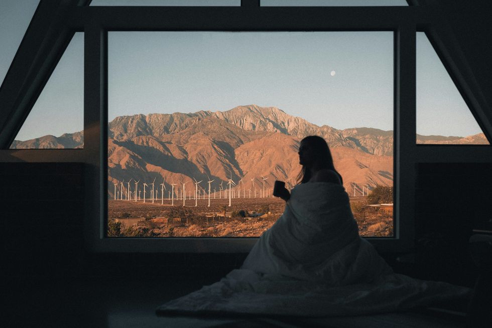 Photo of a woman drinking a cup of coffee while looking at wind turbines in the Californian desert near Palm Springs, U.S.