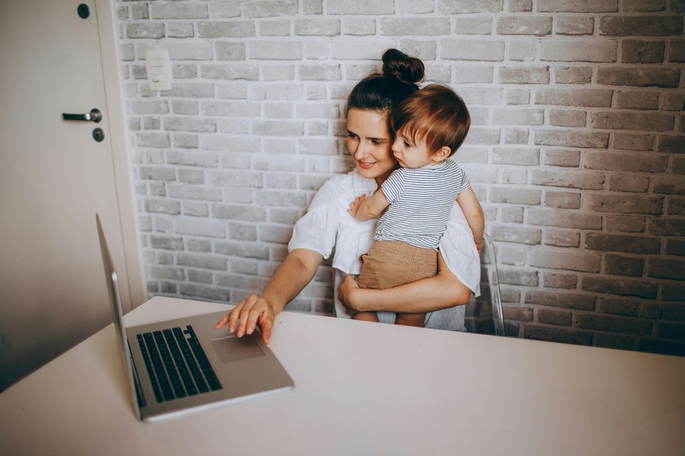 photo of a woman holding a child and working on her computer