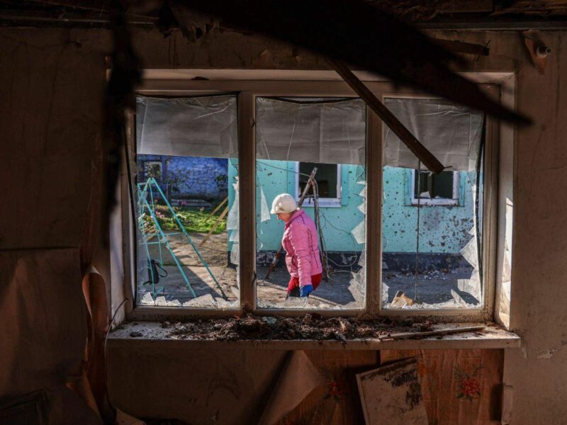 photo of a woman in a pink jacket walking as seen through a blown out window