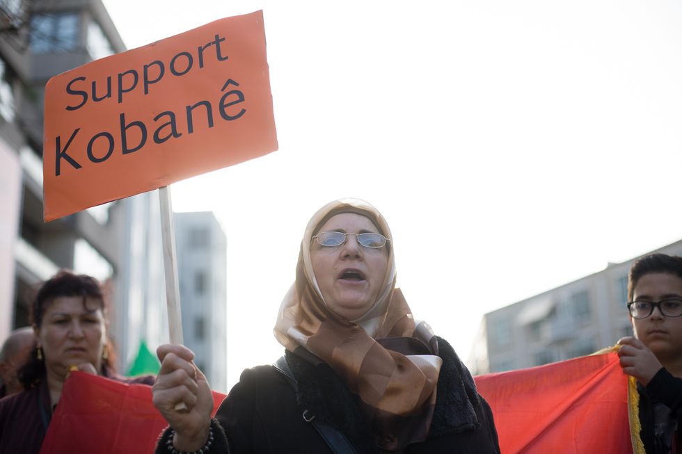 Photo of a woman in a veil marching and holding a sign Kobane