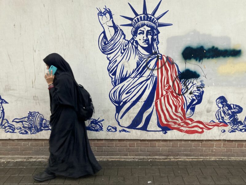 Photo of a woman in Tehran, Iran walking past a mural near the former American Embassy.