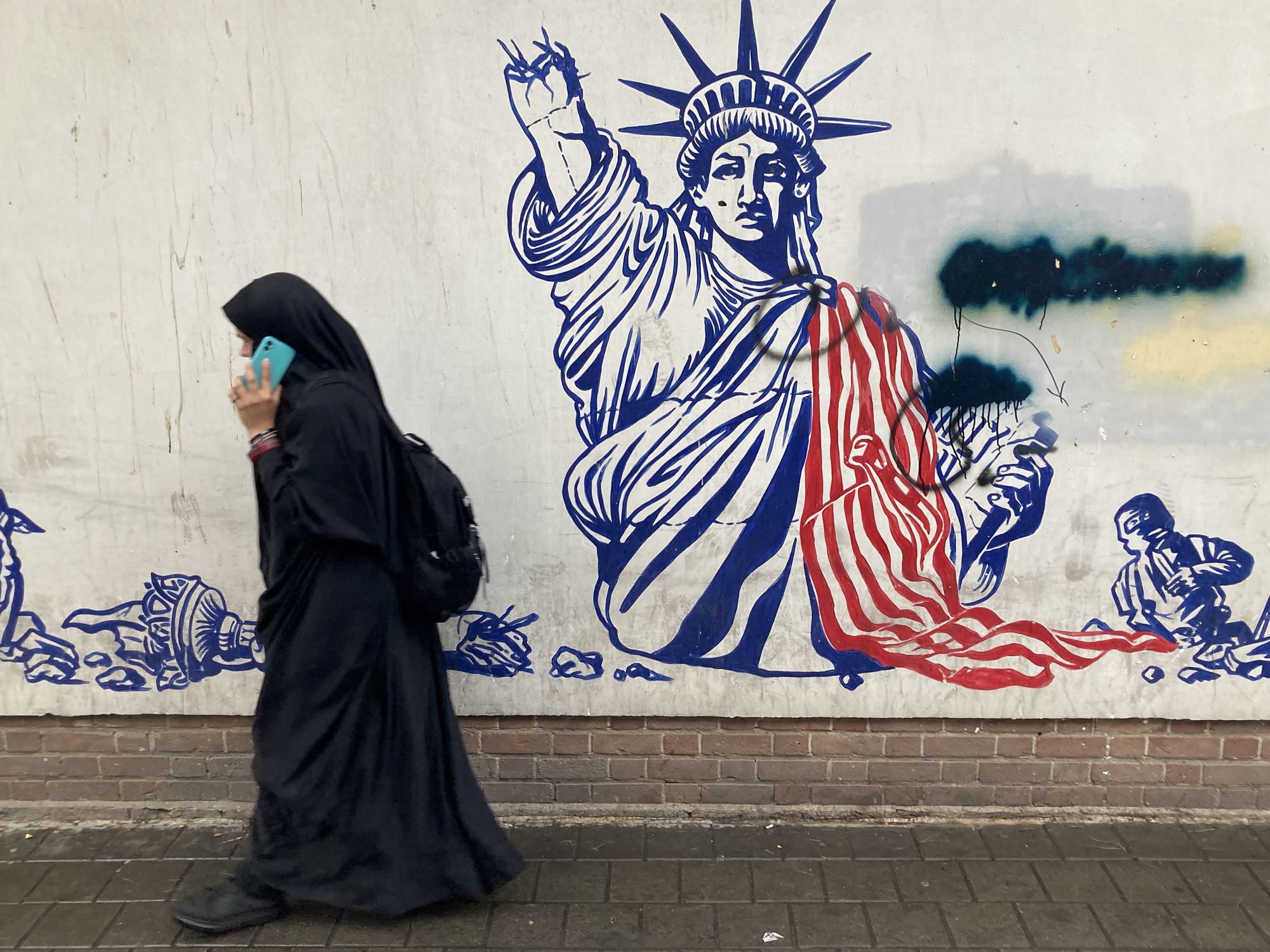 Photo of a woman in Tehran, Iran walking past a mural near the former American Embassy.