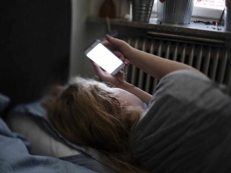 Photo of a woman looking at her phone in her bed