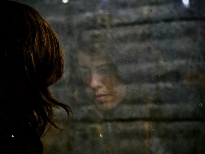 Photo of a woman looking down, with her reflection in a window