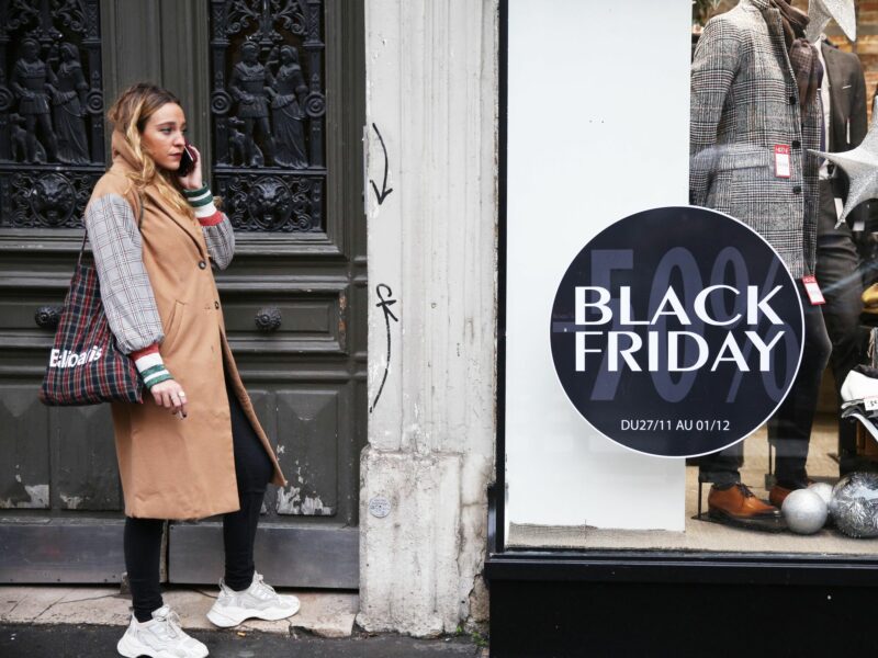 photo of a woman on the phone in front of a storefront with a black friday advertisement