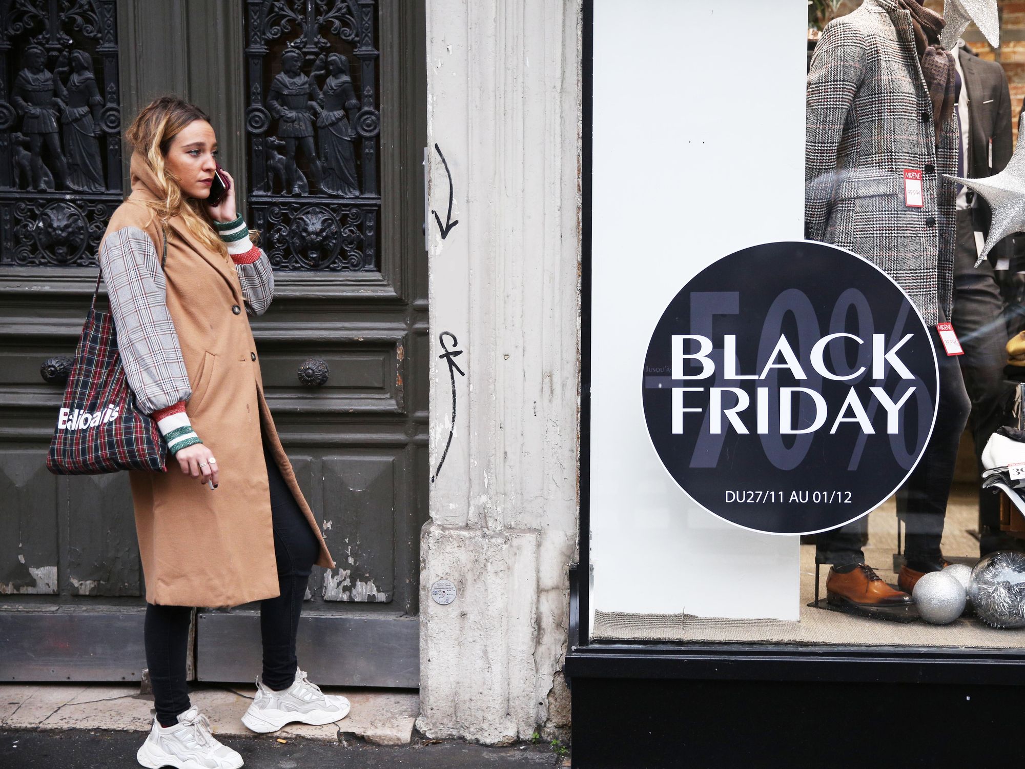 photo of a woman on the phone in front of a storefront with a black friday advertisement
