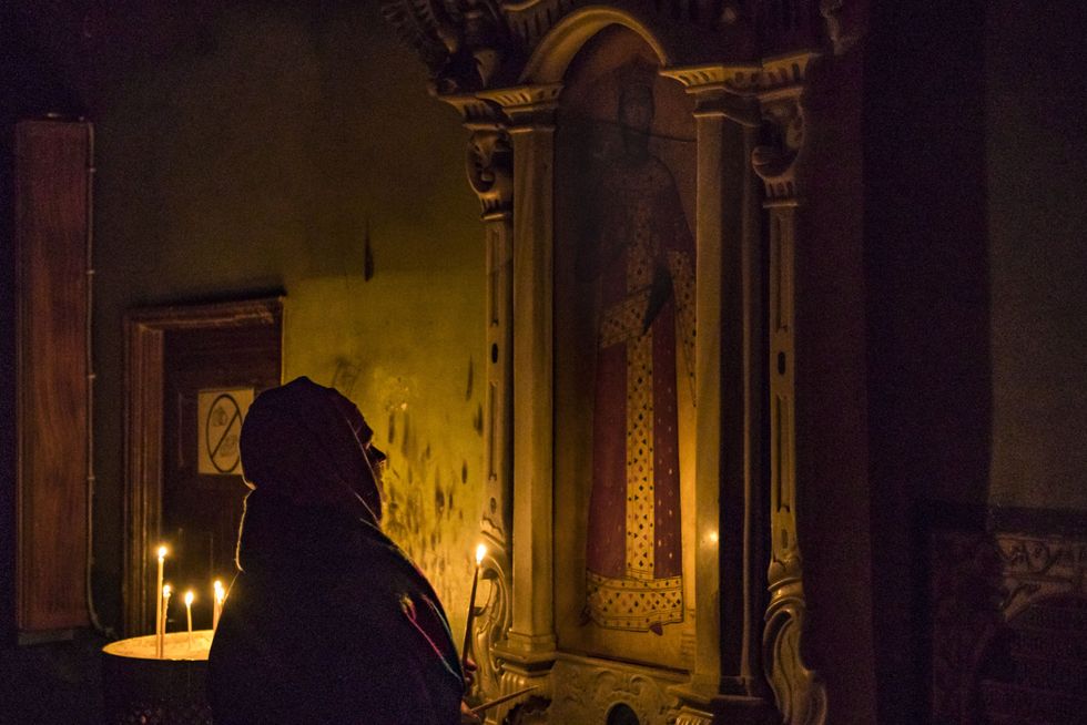 Photo of a woman praying to a saint with a candle during a nightly holy mass for the Epiphany