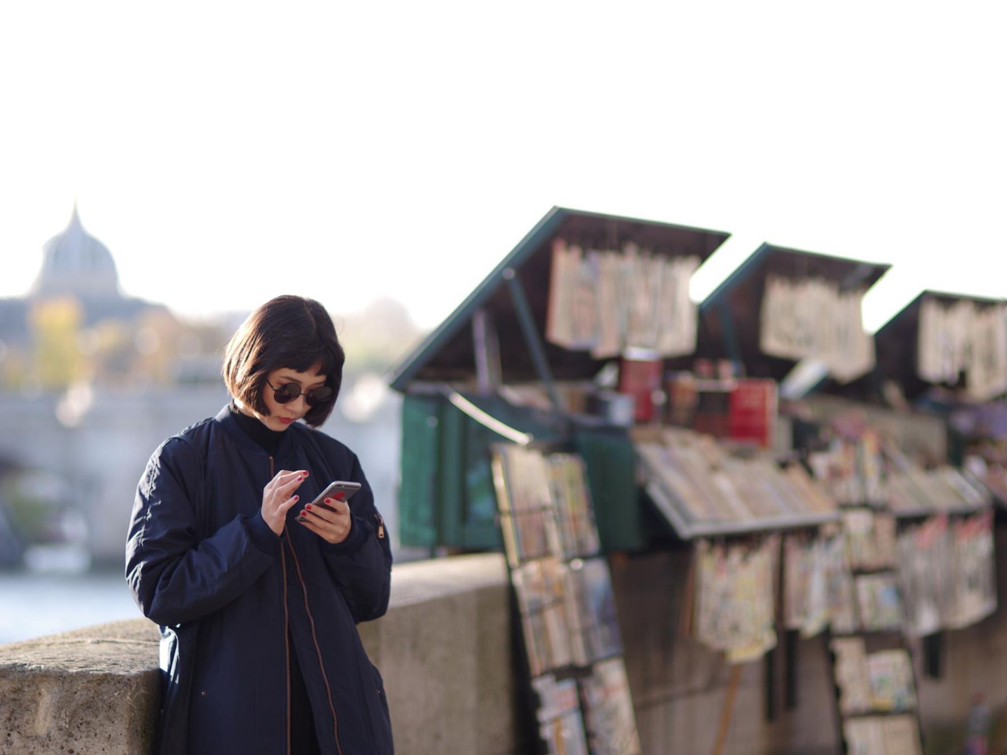 Photo of a woman reading on her smartphone along the banks of the Seine in Paris
