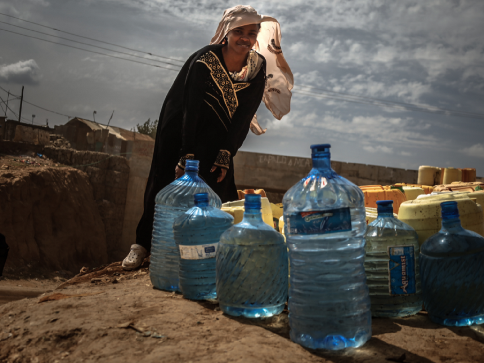 Photo of a woman standing by her water jerrycans during free community water services, amid a clean water shortage in Nairobi's Kibera slum, Kenya.