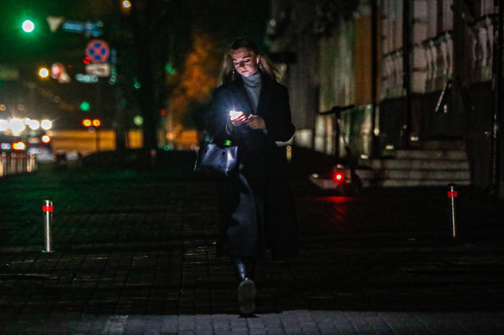 photo of a woman walking a street in kyiv at night holds her phone with the flashlight