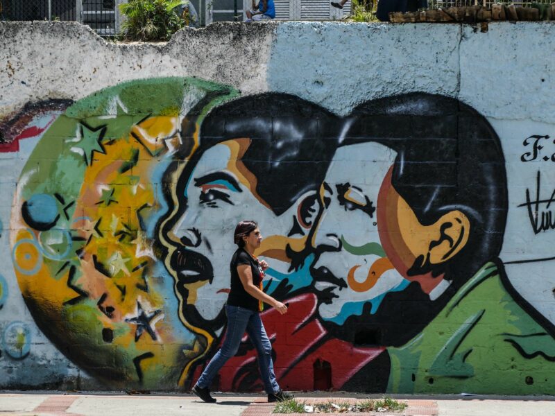 Photo of a woman walking by a wall with street art of Venezuelan presidents Maduro and Chavez in Caracas