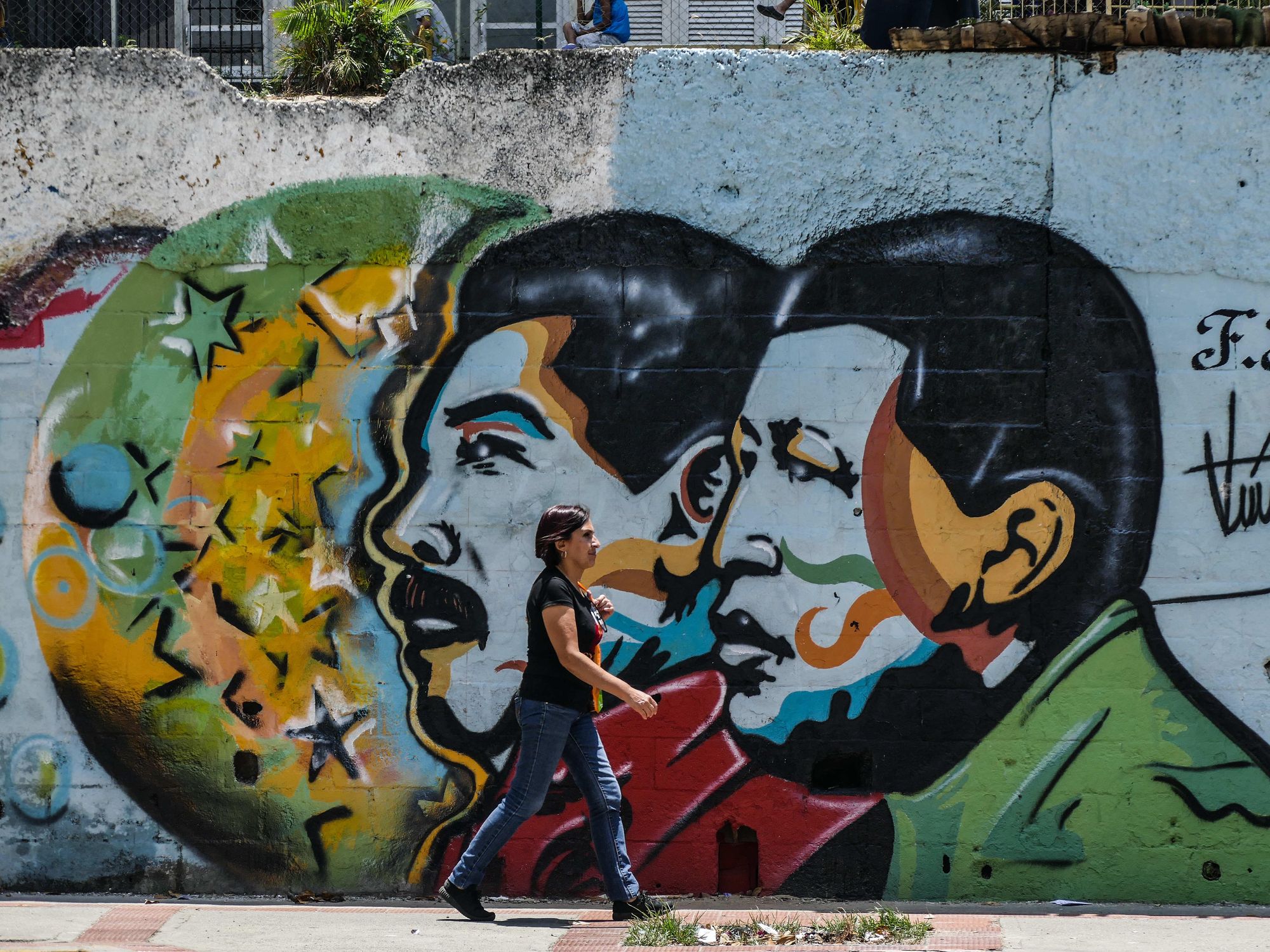 Photo of a woman walking by a wall with street art of Venezuelan presidents Maduro and Chavez in Caracas