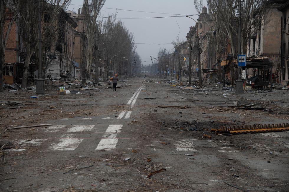 Photo of a woman walking down a destroyed Mariupol street.