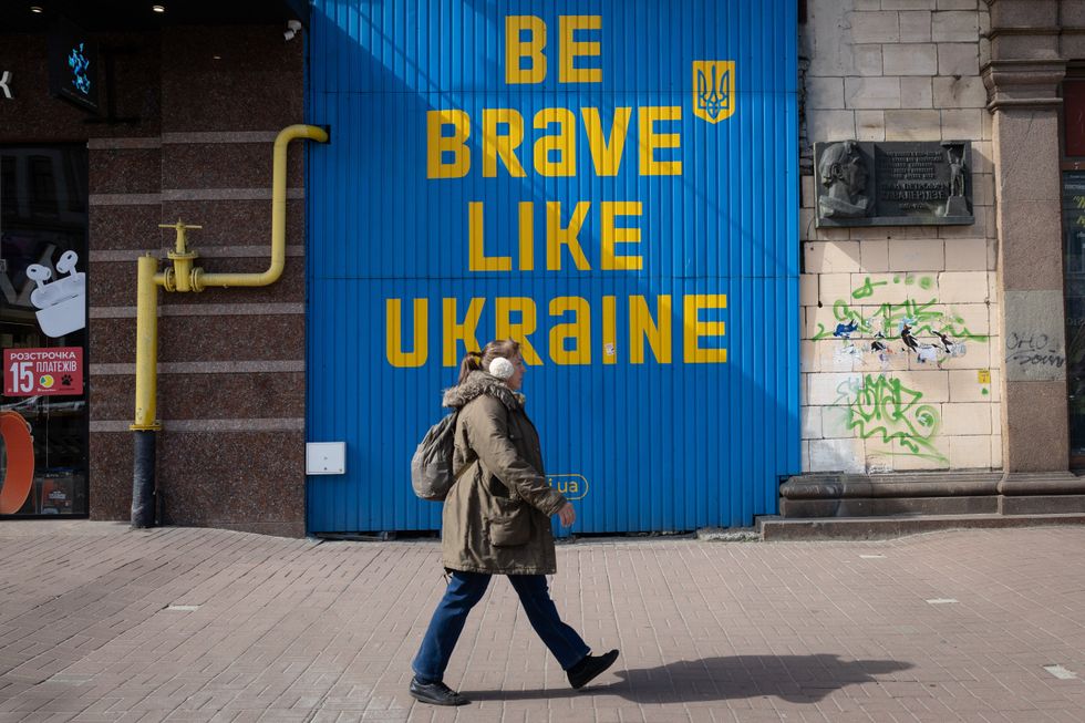 Photo of a woman walking in front of a building with an inscription "be brave in Ukraine"