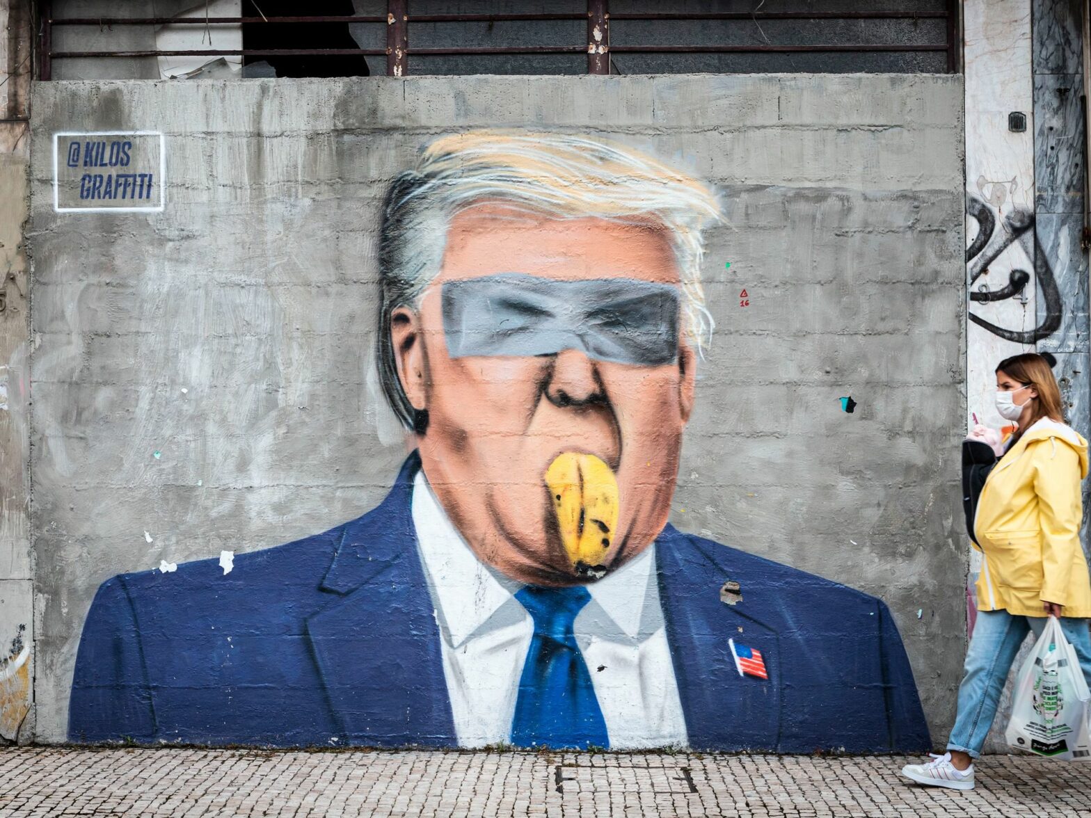 Photo of a woman walking past a graffiti showing Donald Trump with a banana in his mouth, in Porto, Portugal