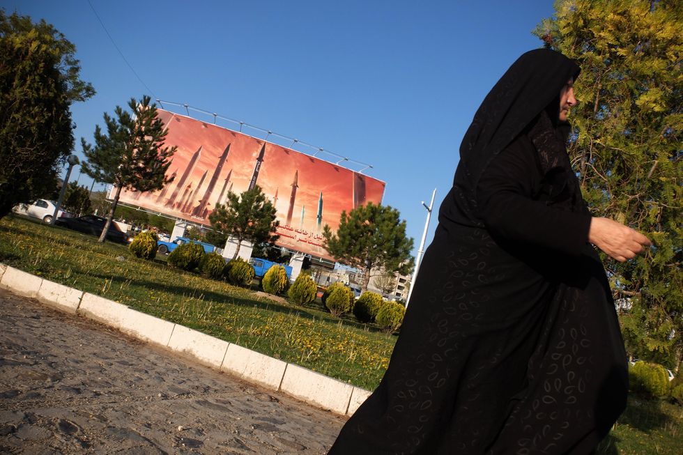 Photo of a woman walking past an anti-Israel billboard carrying pictures of Iranian missiles in Iran.