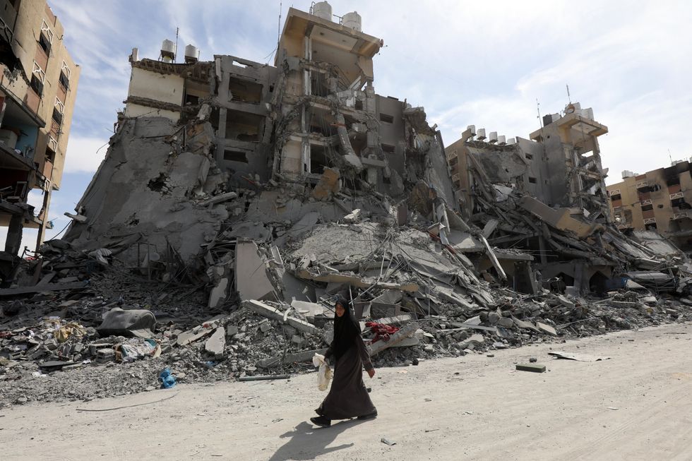 Photo of a woman walking past destroyed buildings in Hamad City, Gaza.
