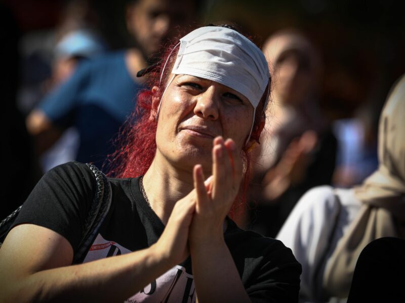 photo of a woman with a covid mask on her forehead clapping at an anti-vaccination protest in Ankara, Turkey