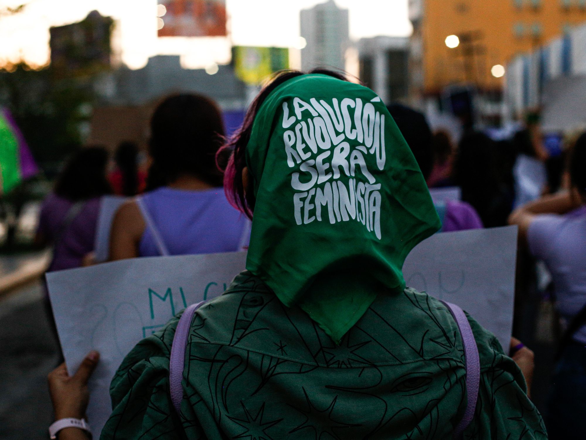 photo of a woman with a green scarf that says: ​"The Revolution will be Feminist"
