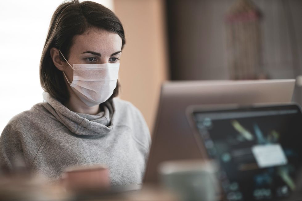 Photo of a woman working on a computer while wearing a COVID mask