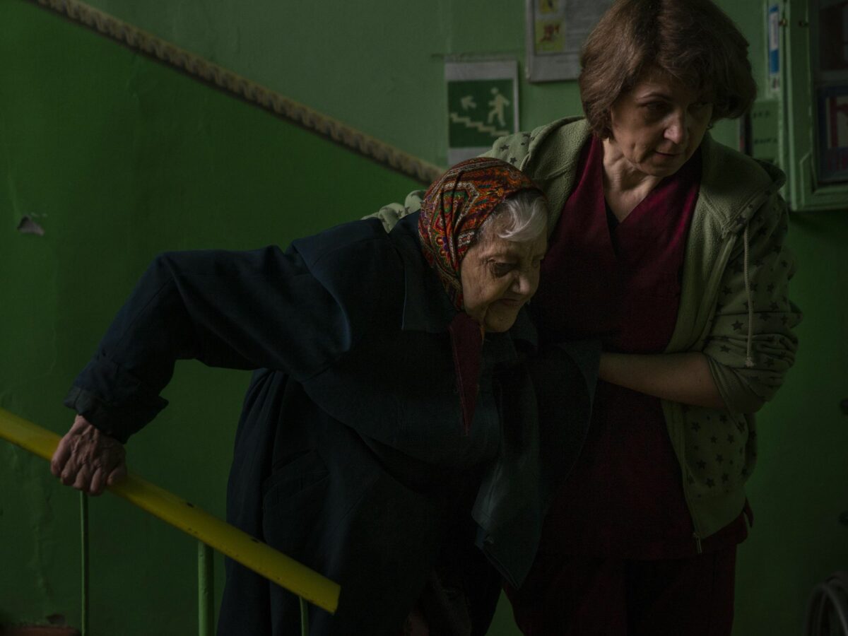 Photo of a worker assisting a resident down a stairwell at an elderly residential center, to evacuate her from Toretsk, Ukraine on April 13,​