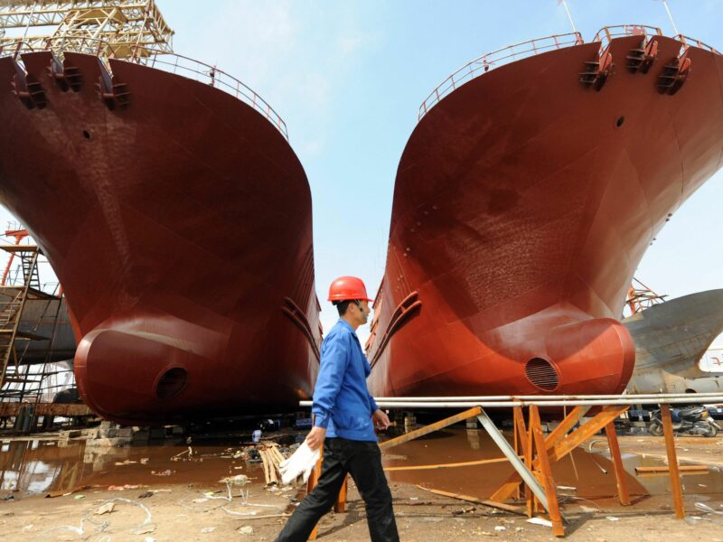 Photo of a worker walking past two ships in a shipyard in Taizhou, China