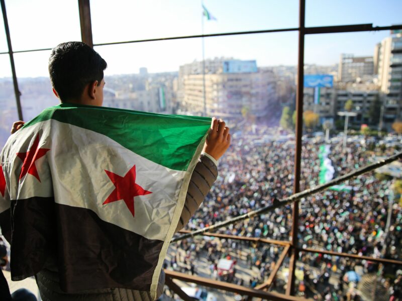 Photo of a young boy carrying the Syrian flag on his bag during a rally in Aleppo celebrating the fall of Bashar Al-Assad.