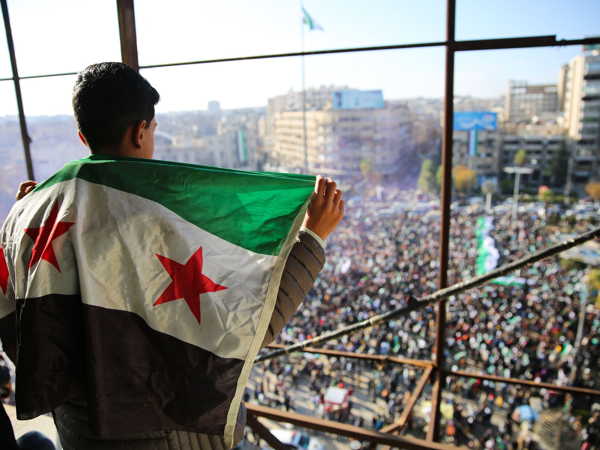 Photo of a young boy carrying the Syrian flag on his bag during a rally in Aleppo celebrating the fall of Bashar Al-Assad.