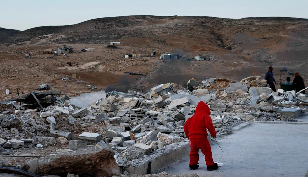 Photo of a young child standing in the rubble of a destroyed home.