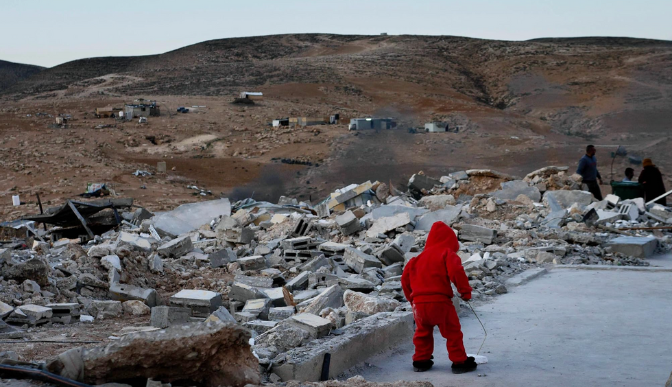 Photo of a young child standing in the rubble of a destroyed home.