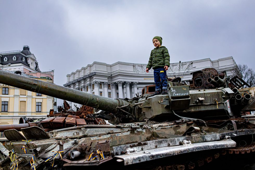 Photo of a young child standing on top of a destroyed tank in Kyiv