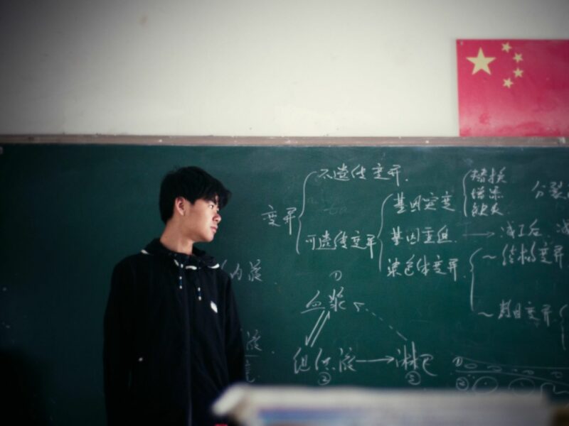 Photo of a young Chinese man looking at a blackboard with a flag of China above