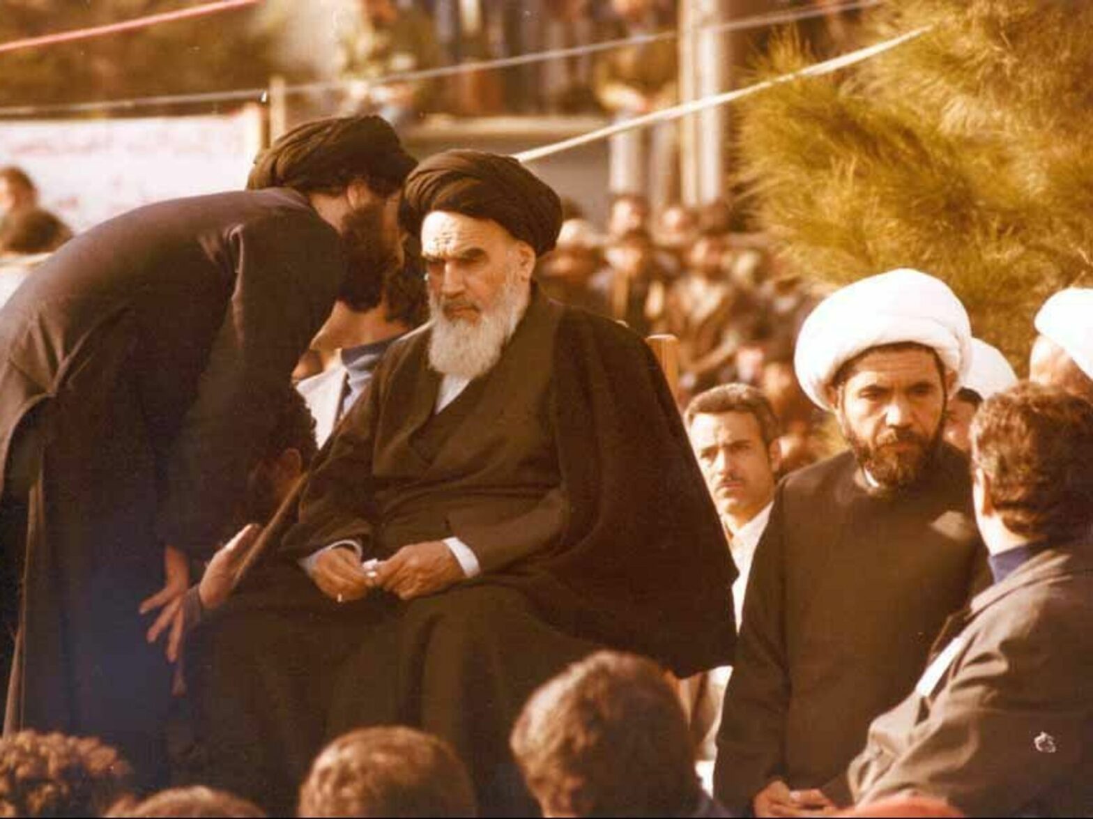 photo of a young cleric talking into the ear of the Ayatollah